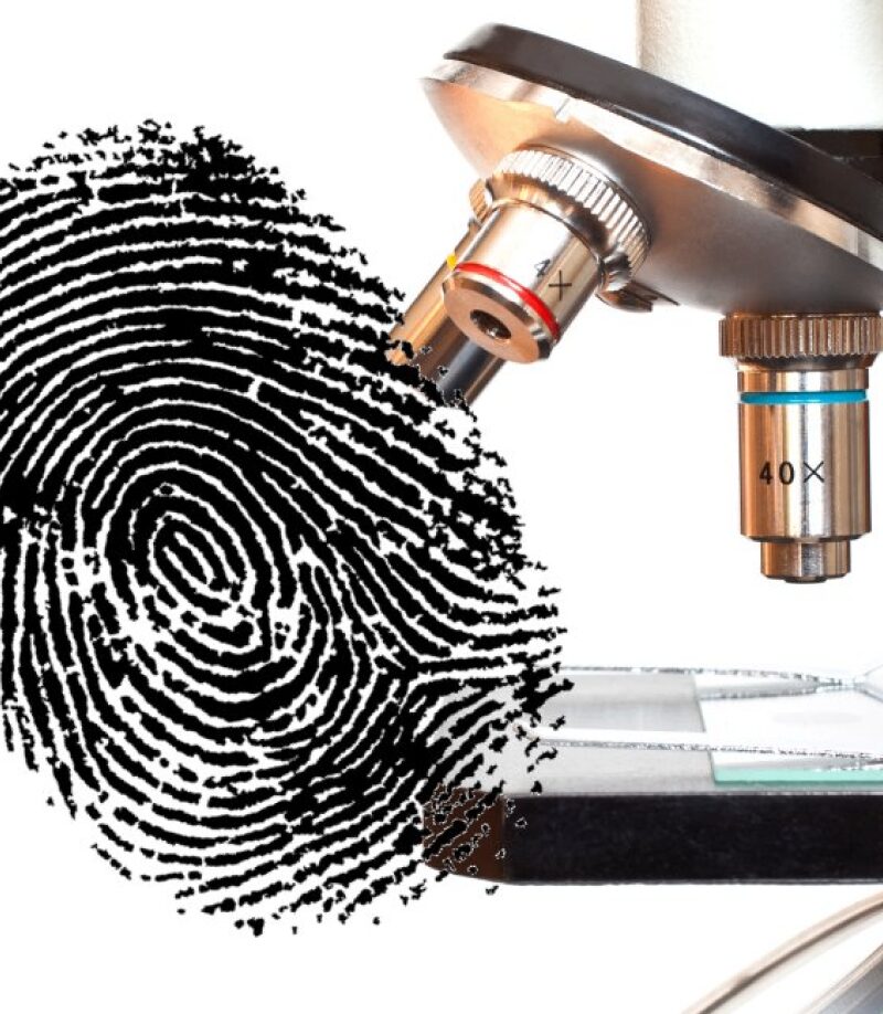 A microscope lens positioned over a large, black fingerprint on a glass slide, illustrating forensic analysis.