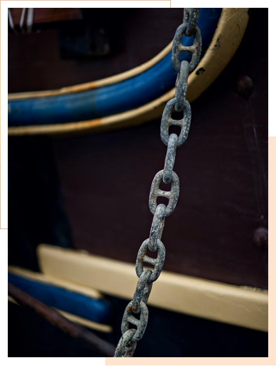 A close-up of a rusty metal chain hanging in front of a wooden surface with blue and yellow painted details.